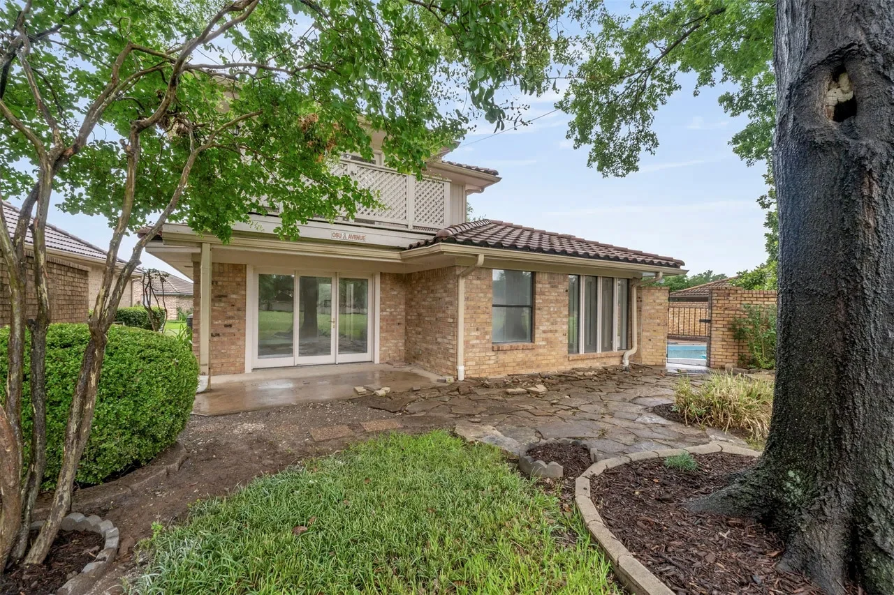 Raised patio and landscaped poolside exterior behind a brick Fort Worth home with mature trees in Fort Worth, Texas.