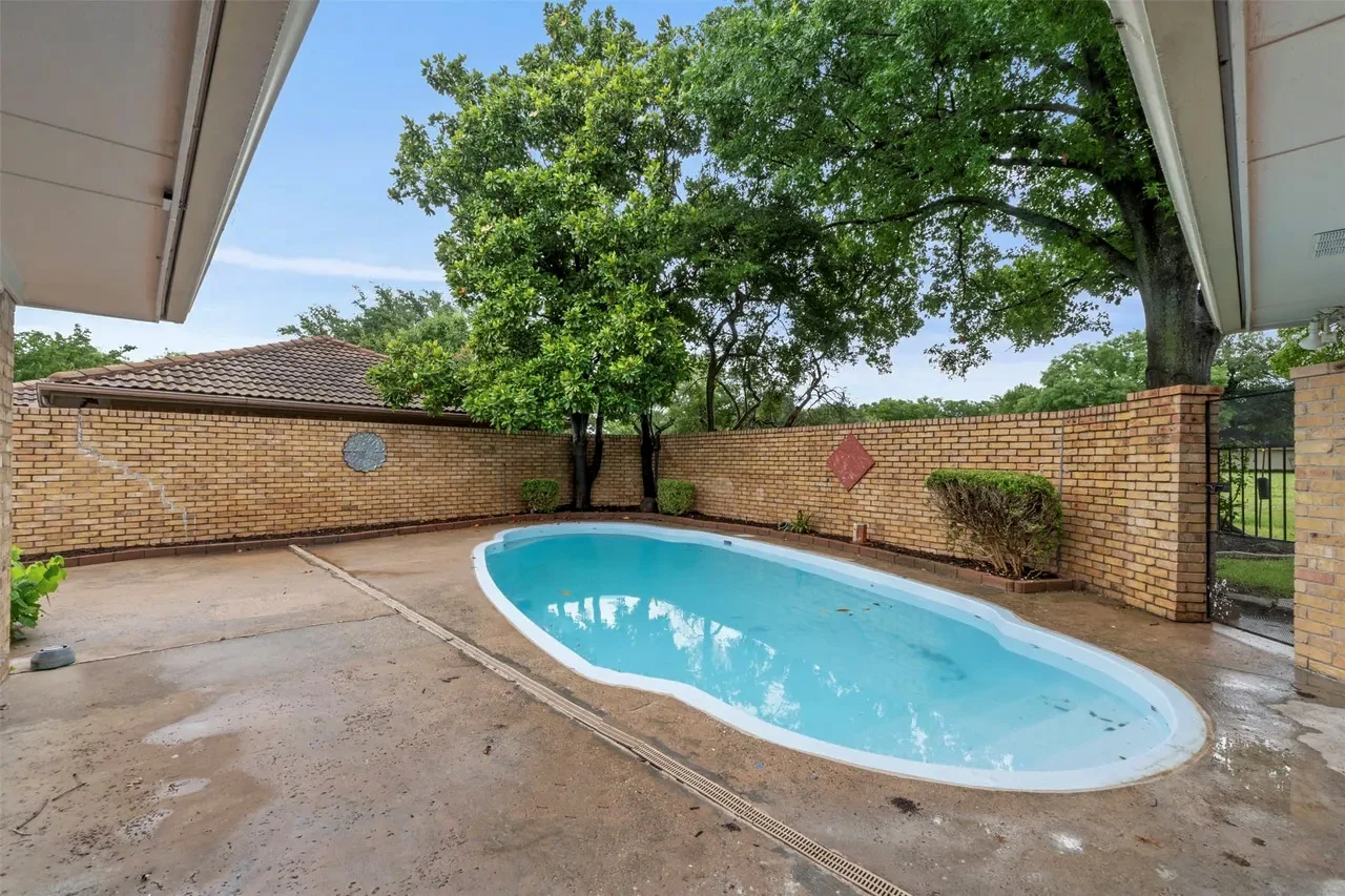 Refinished backyard swimming pool with clean blue water, surrounding concrete deck, brick privacy wall, and shade trees in Fort Worth, Texas.