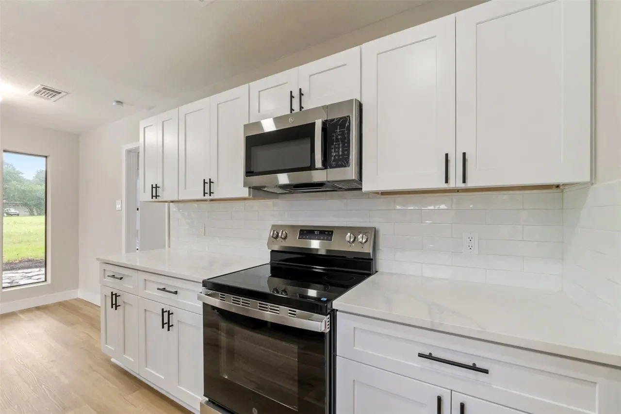 White shaker kitchen with stainless steel appliances, black hardware, subway tile backsplash, and wood-look flooring in Fort Worth, Texas.
