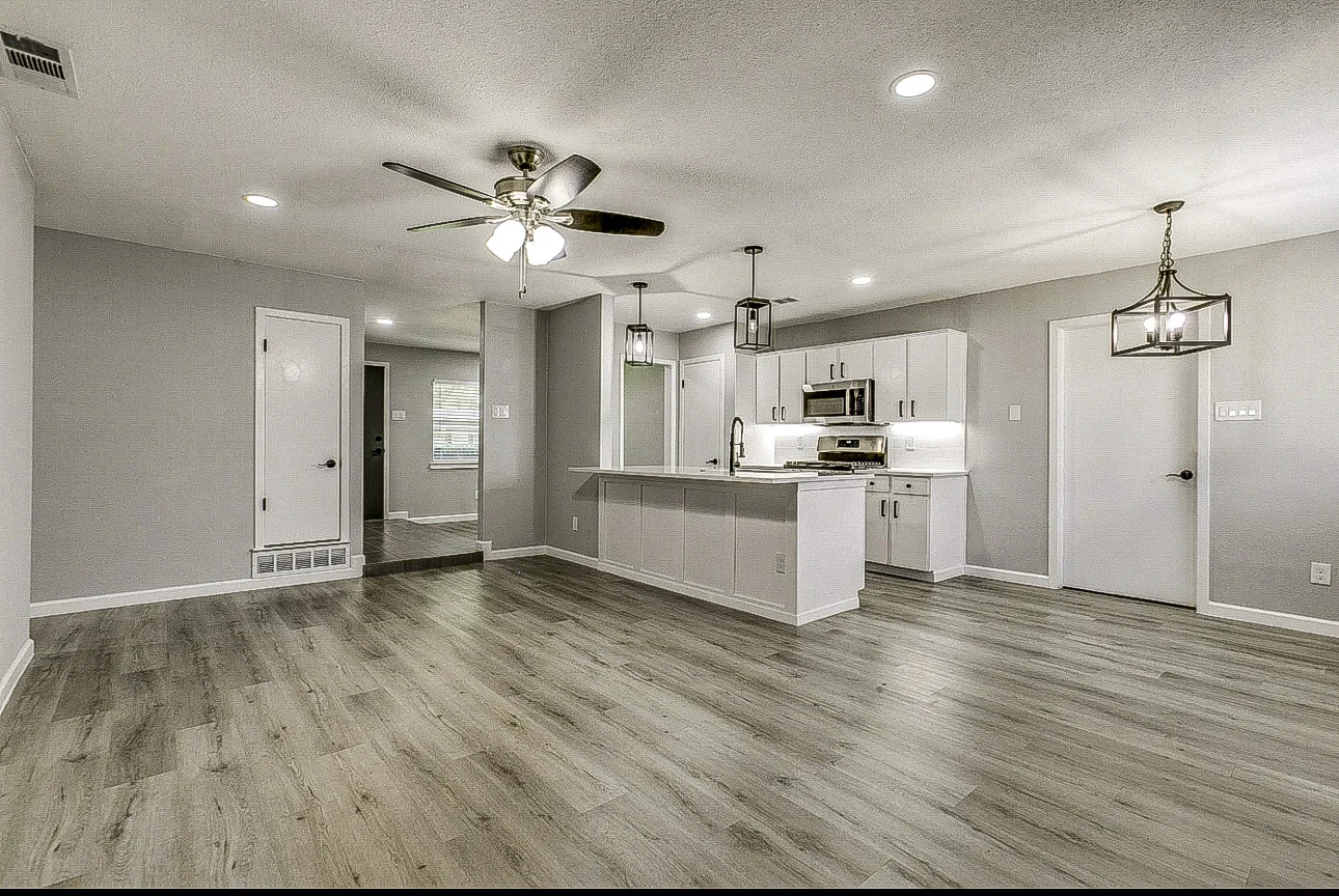 Open kitchen and living room with white cabinets, peninsula seating, gray walls, and wood-look flooring in Garland.