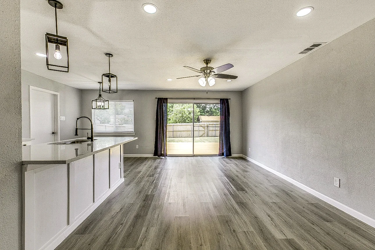 Open living and dining room with gray walls, peninsula cabinetry, sliding glass door, and wood-look flooring in Garland.