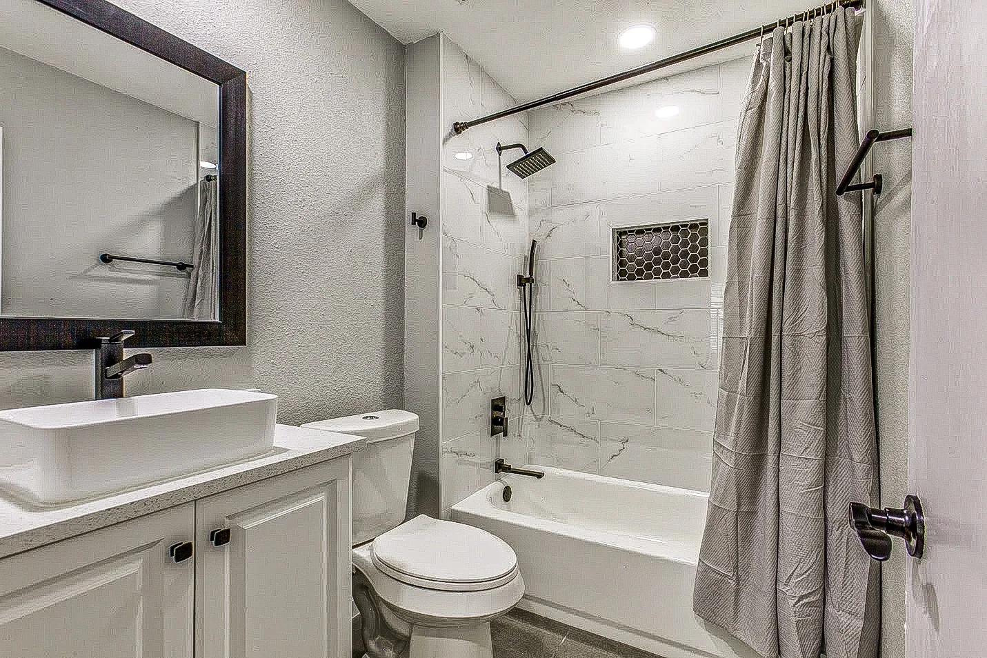 Guest bathroom with white vanity, black fixtures, marble-look tub surround, and glass panel in Garland.