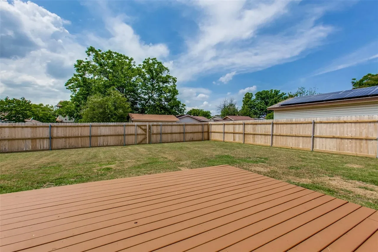 New backyard deck and wood privacy fence with an open lawn and clear views from the remodeled living area in Garland, Texas.