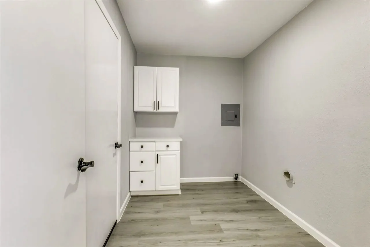 Updated electrical panel and utility room with new flooring, white storage cabinetry, and finished walls in Garland, Texas.