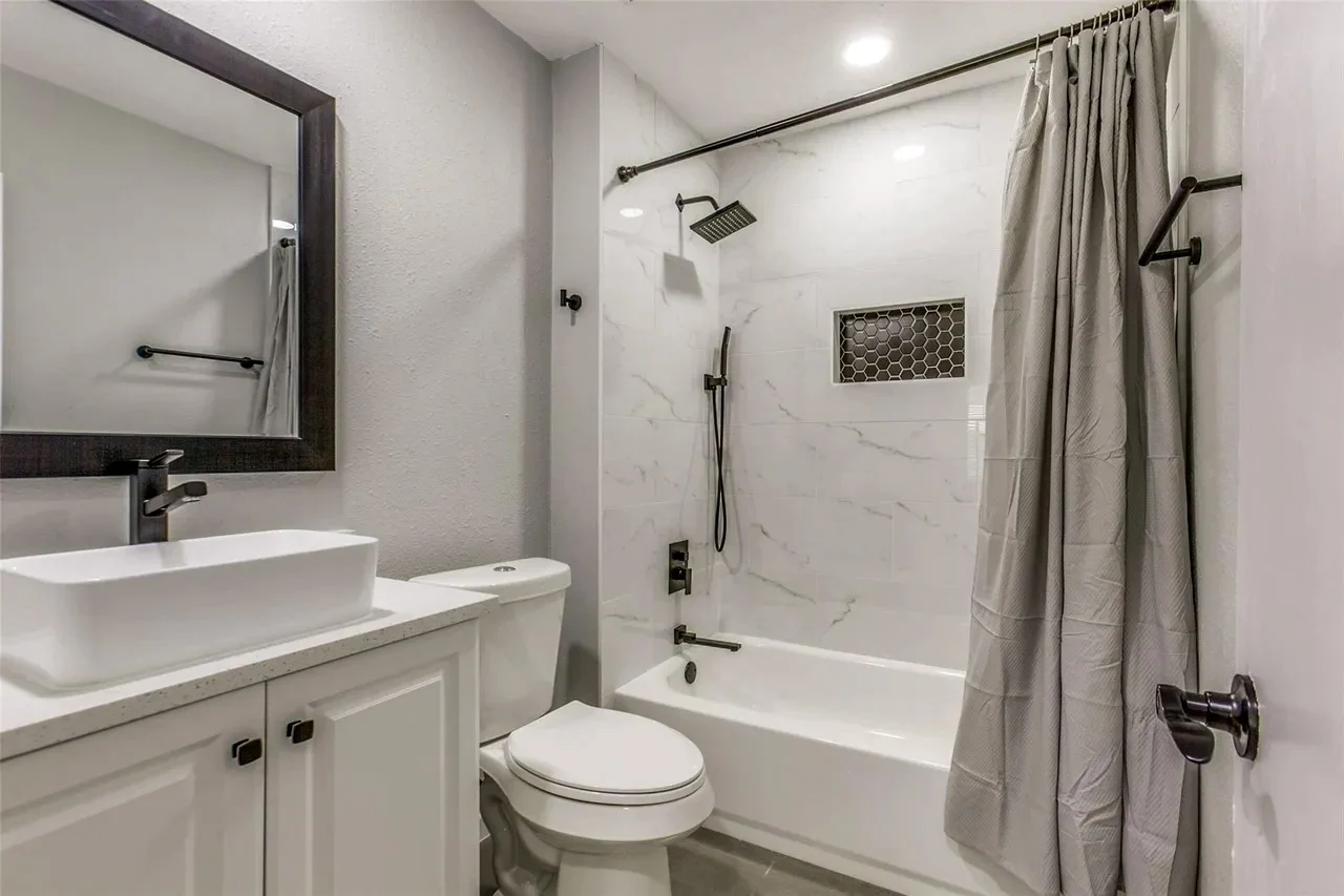Guest bathroom with a marble-look tub surround, white vessel sink, white vanity, black fixtures, and gray walls in Garland, Texas.