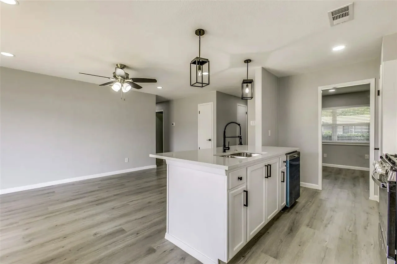 Open-concept kitchen and living area after wall removal with a white island, black fixtures, pendant lights, and gray flooring in Garland, Texas.