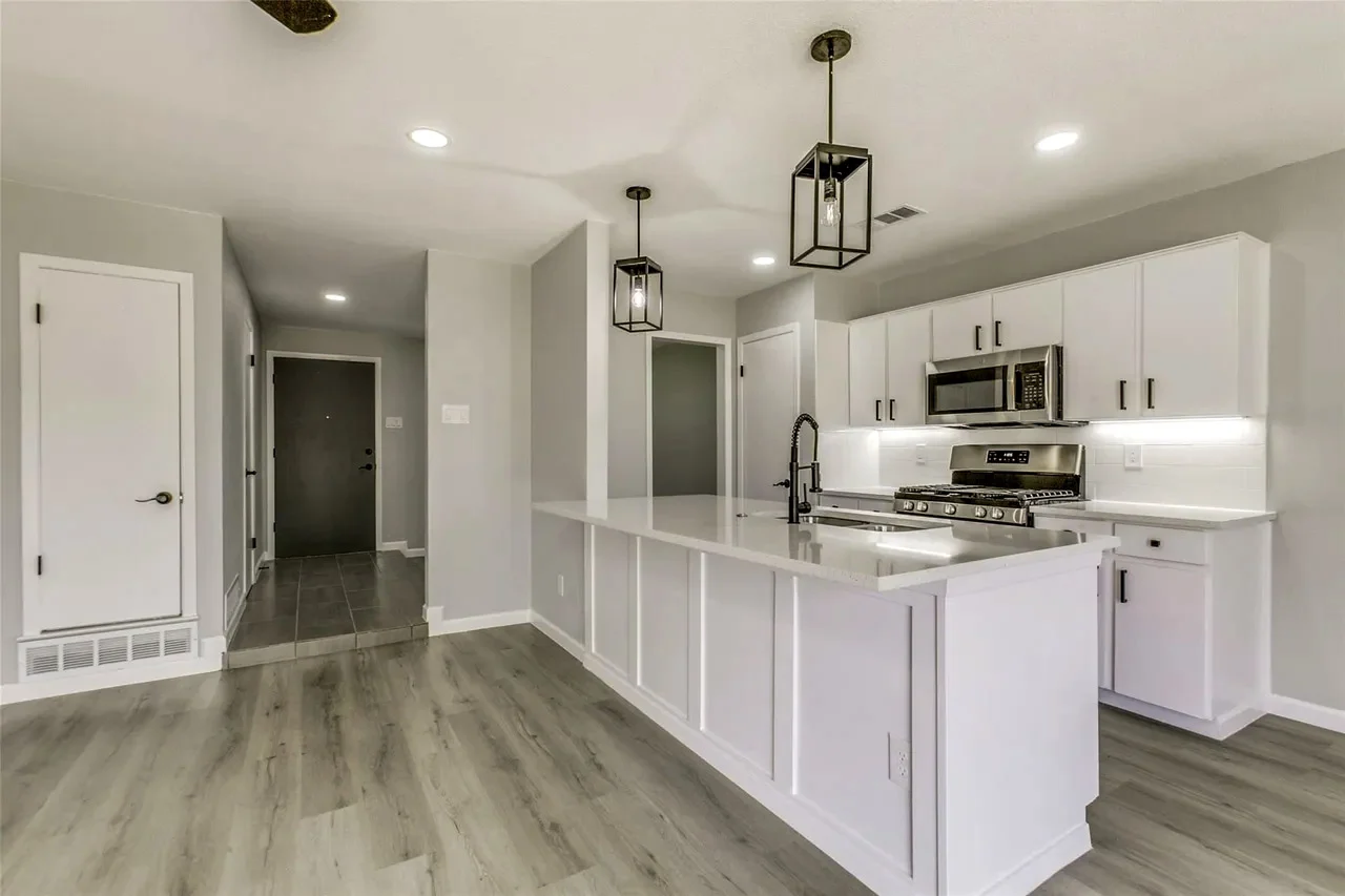 Wide open kitchen and living area after structural wall removal with white cabinetry, an island, and gray wood-look flooring in Garland, Texas.
