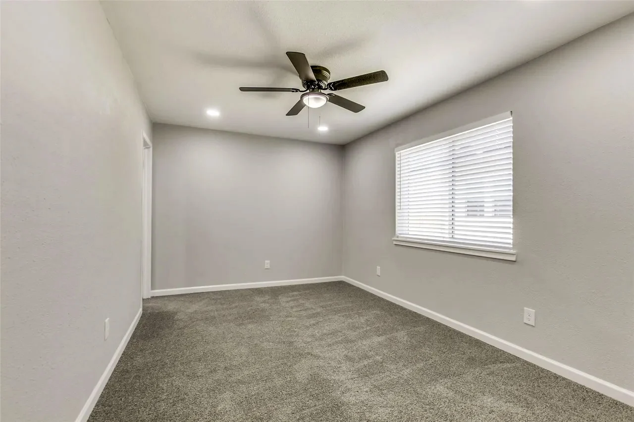 Primary bedroom with new carpet, light gray walls, white trim, wide window, and ceiling fan in Garland, Texas.