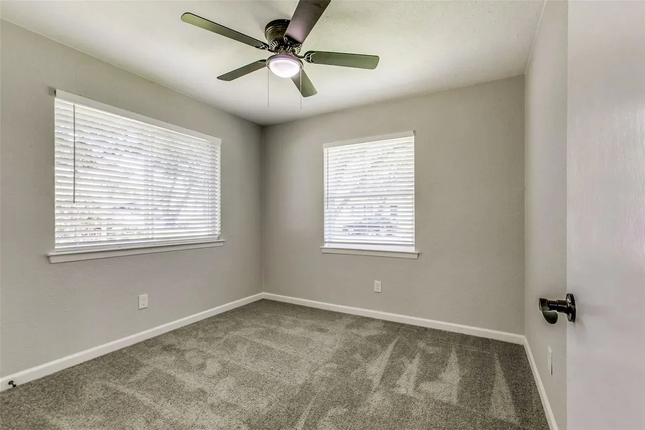 Corner secondary bedroom with new carpet, light gray walls, two windows, white trim, and ceiling fan in Garland, Texas.