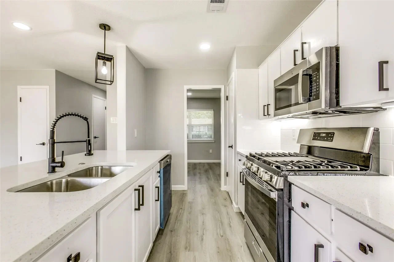 White galley kitchen with a black pull-down faucet, stainless steel range, black hardware, and under-cabinet lighting in Garland, Texas.