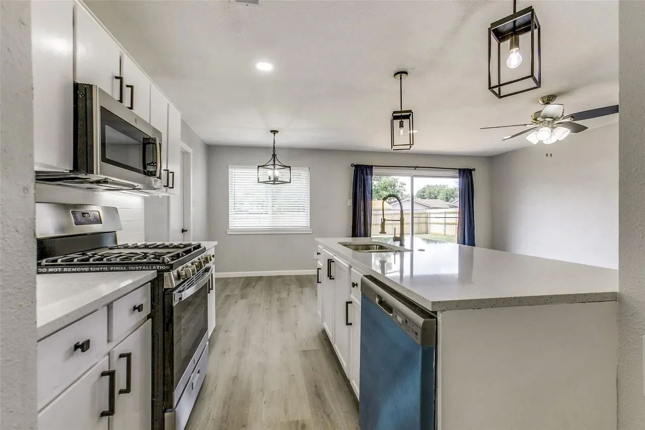 White kitchen with a center island, stainless steel range, black hardware, pendant lighting, and gray wood-look flooring in Garland, Texas.