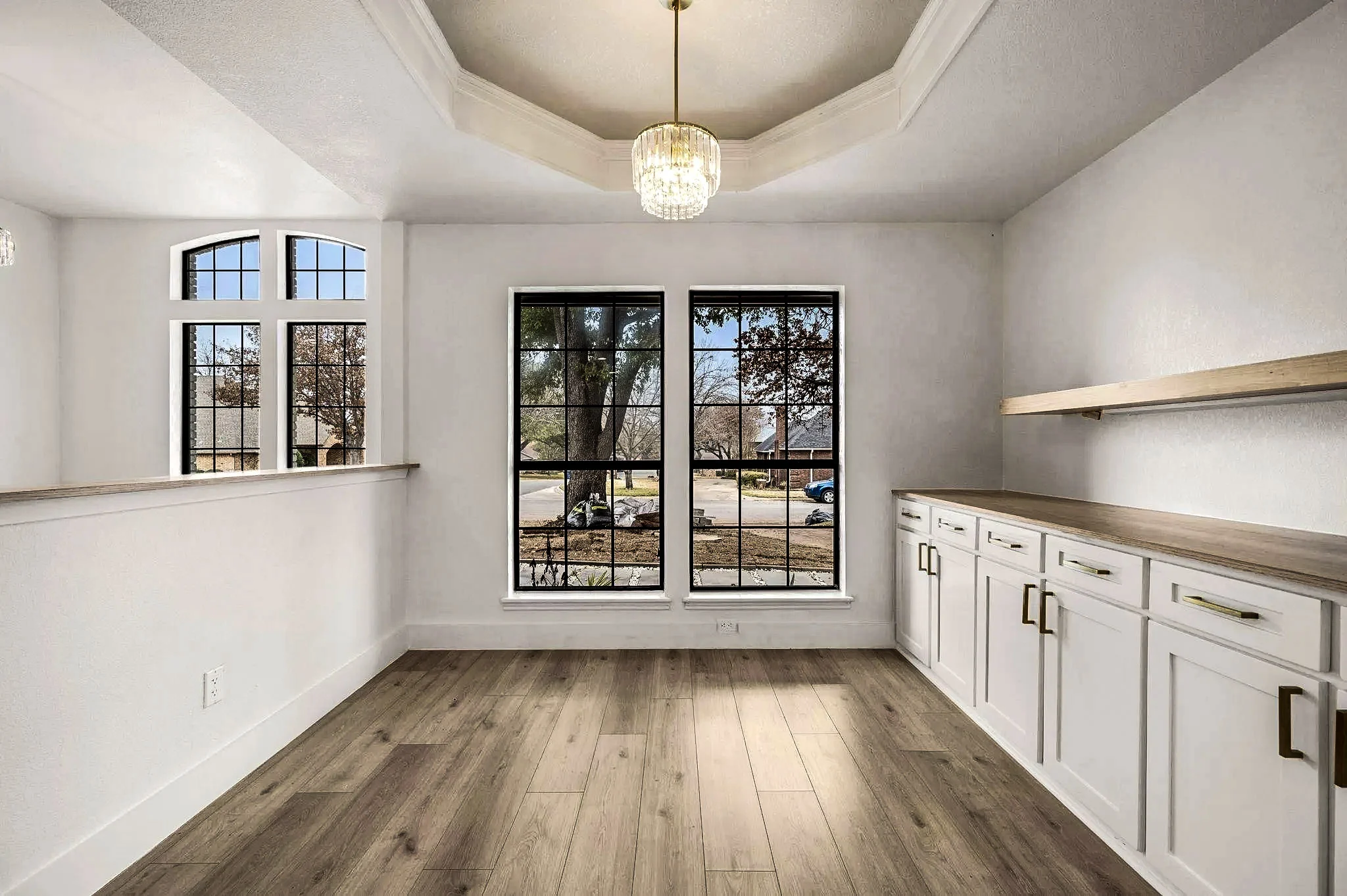Breakfast room with arched black-framed windows, white built-in cabinetry, open shelving, and wood-look flooring in Grapevine, Texas.
