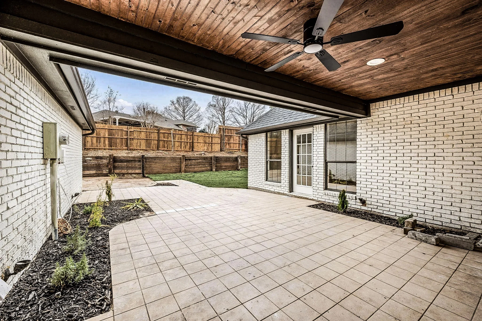 Covered backyard patio with a stained wood ceiling, ceiling fans, pavers, and white brick exterior walls in Grapevine, Texas.