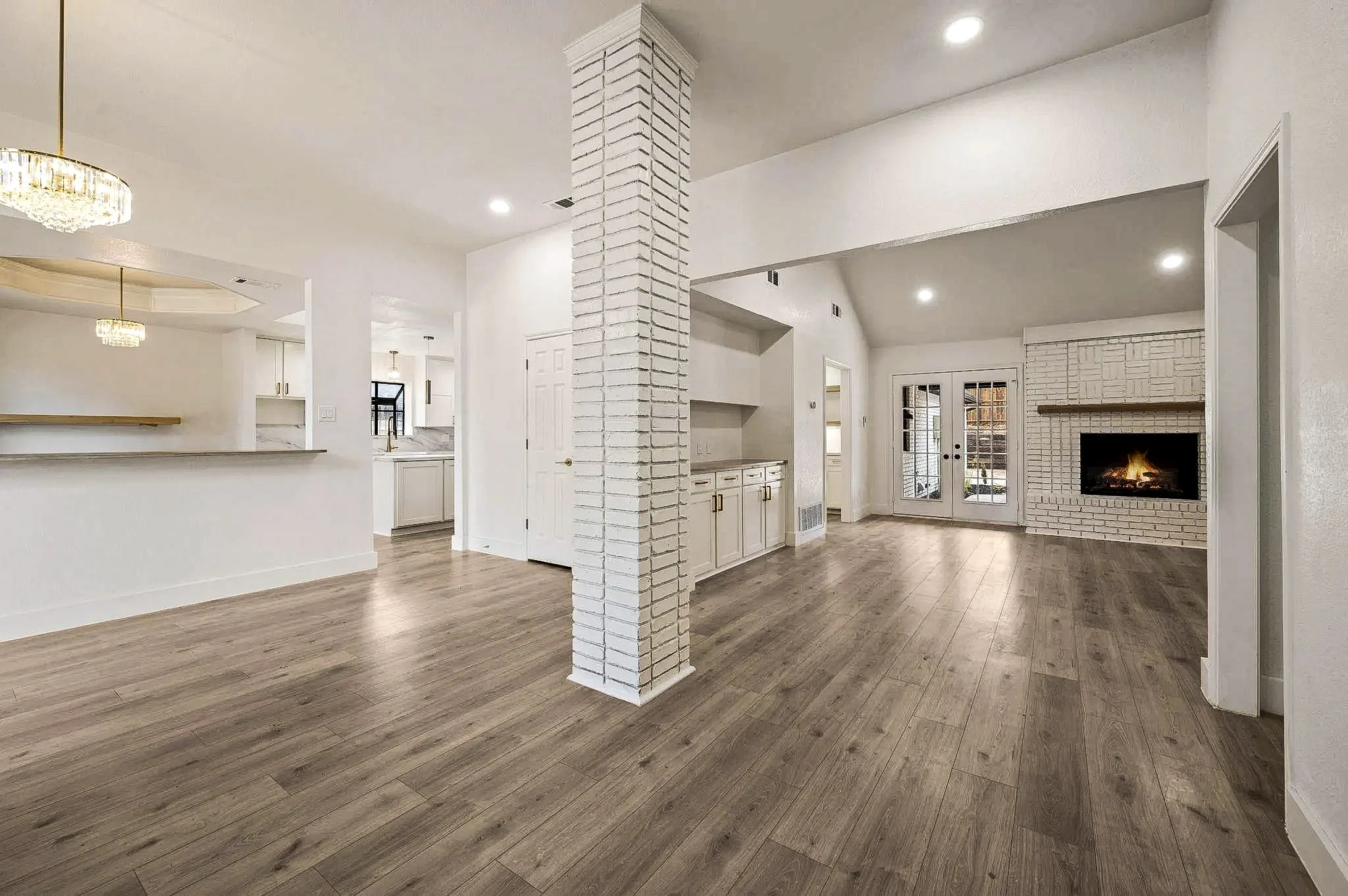 Open dining and entry area with a white brick column, custom cabinetry, black-framed doors, and wide-plank flooring in Grapevine, Texas.