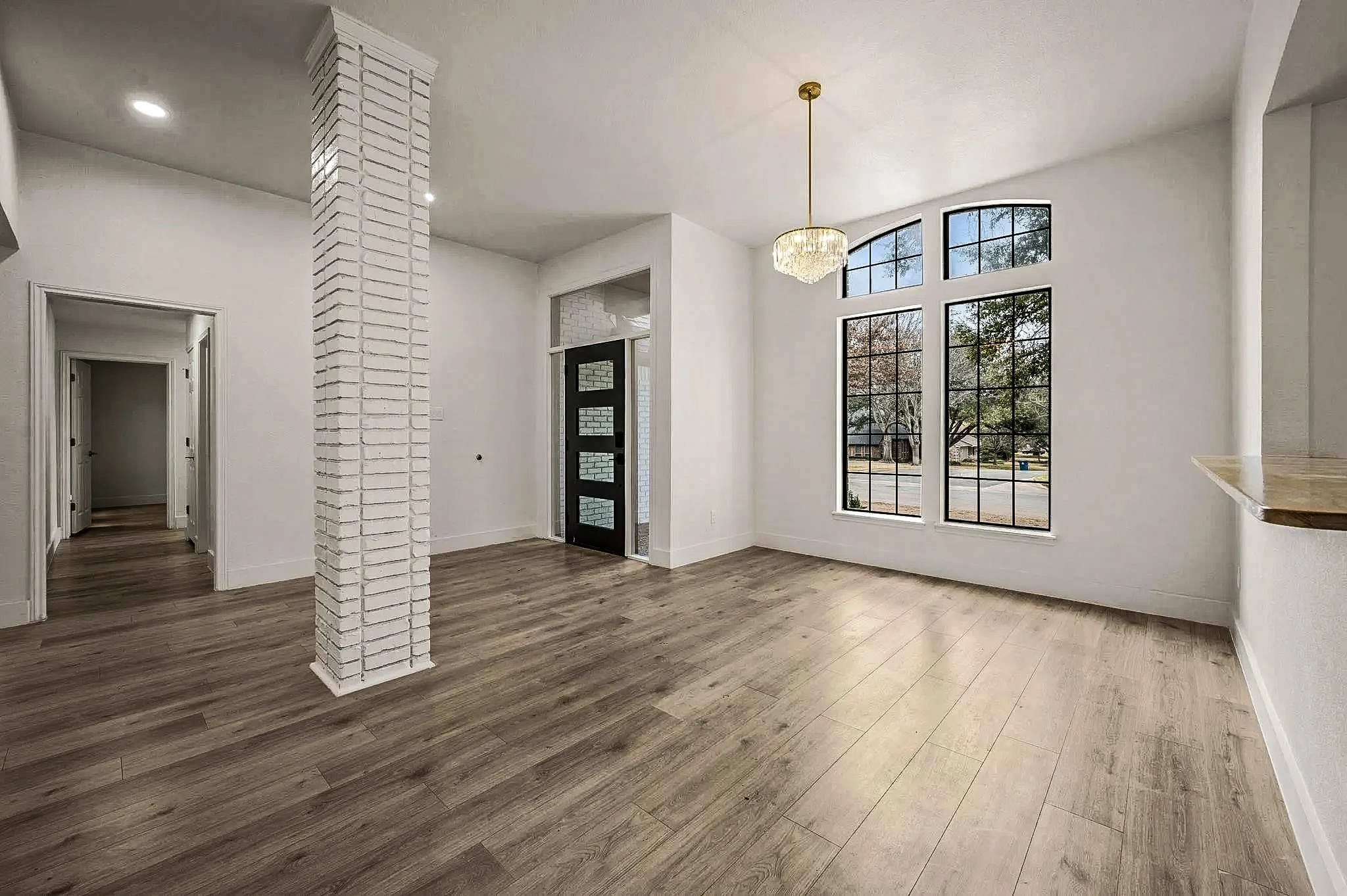 Dining room with a white brick column, black-framed windows, modern chandelier, and wide-plank flooring in Grapevine, Texas.