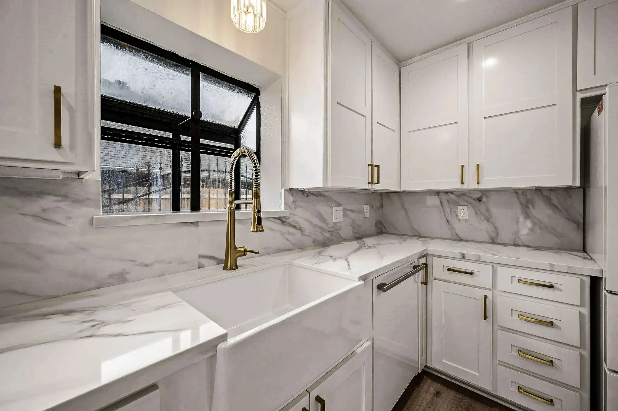 White kitchen with a farmhouse sink, black-framed window, brass faucet, marble-look backsplash, and built-in storage in Grapevine, Texas.
