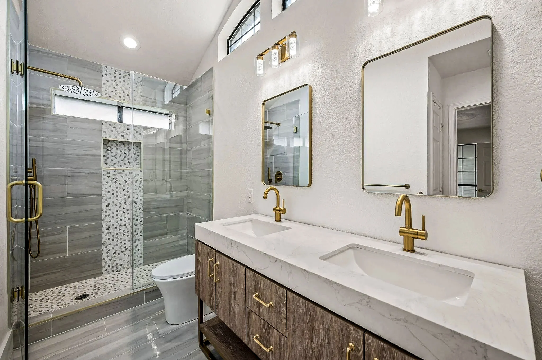 Jack-and-Jill bathroom with a wood double vanity, white counters, brass fixtures, glass shower, and patterned tile in Grapevine, Texas.