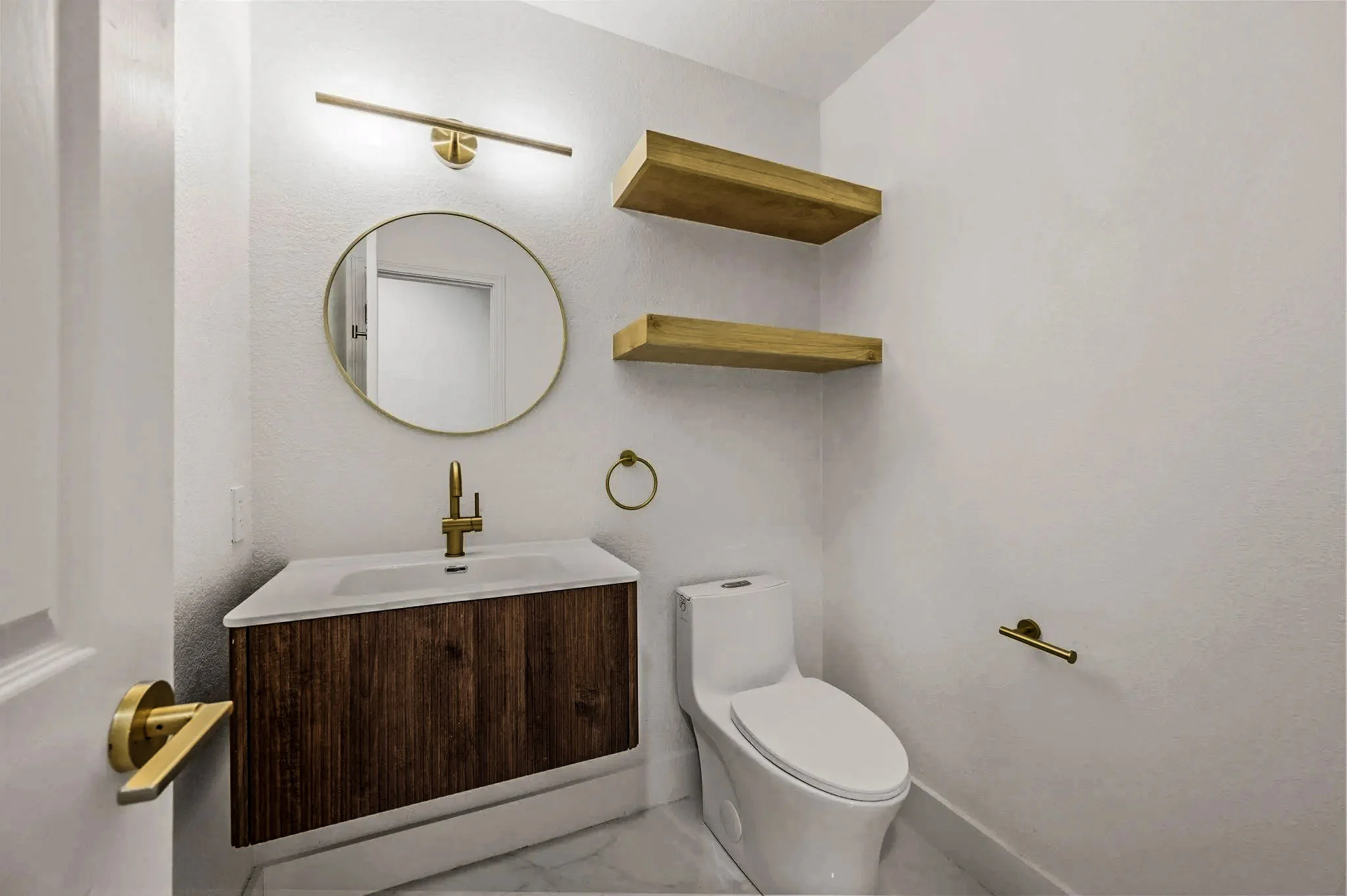 Powder room with a floating walnut vanity, round mirror, brass fixtures, and open brass shelving in Grapevine, Texas.
