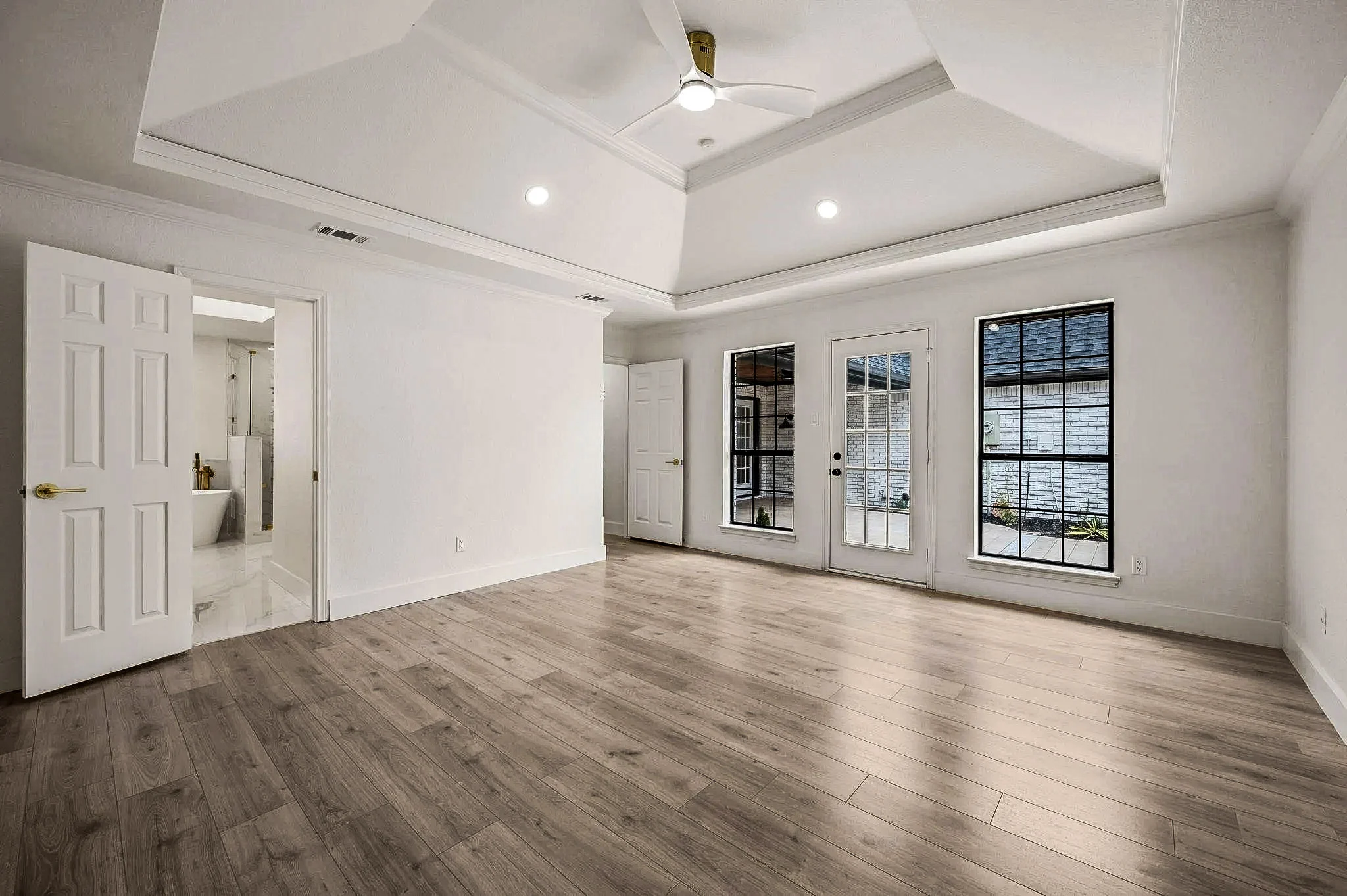 Primary bedroom with a tray ceiling, French doors, black-framed windows, and wide-plank flooring in Grapevine, Texas.