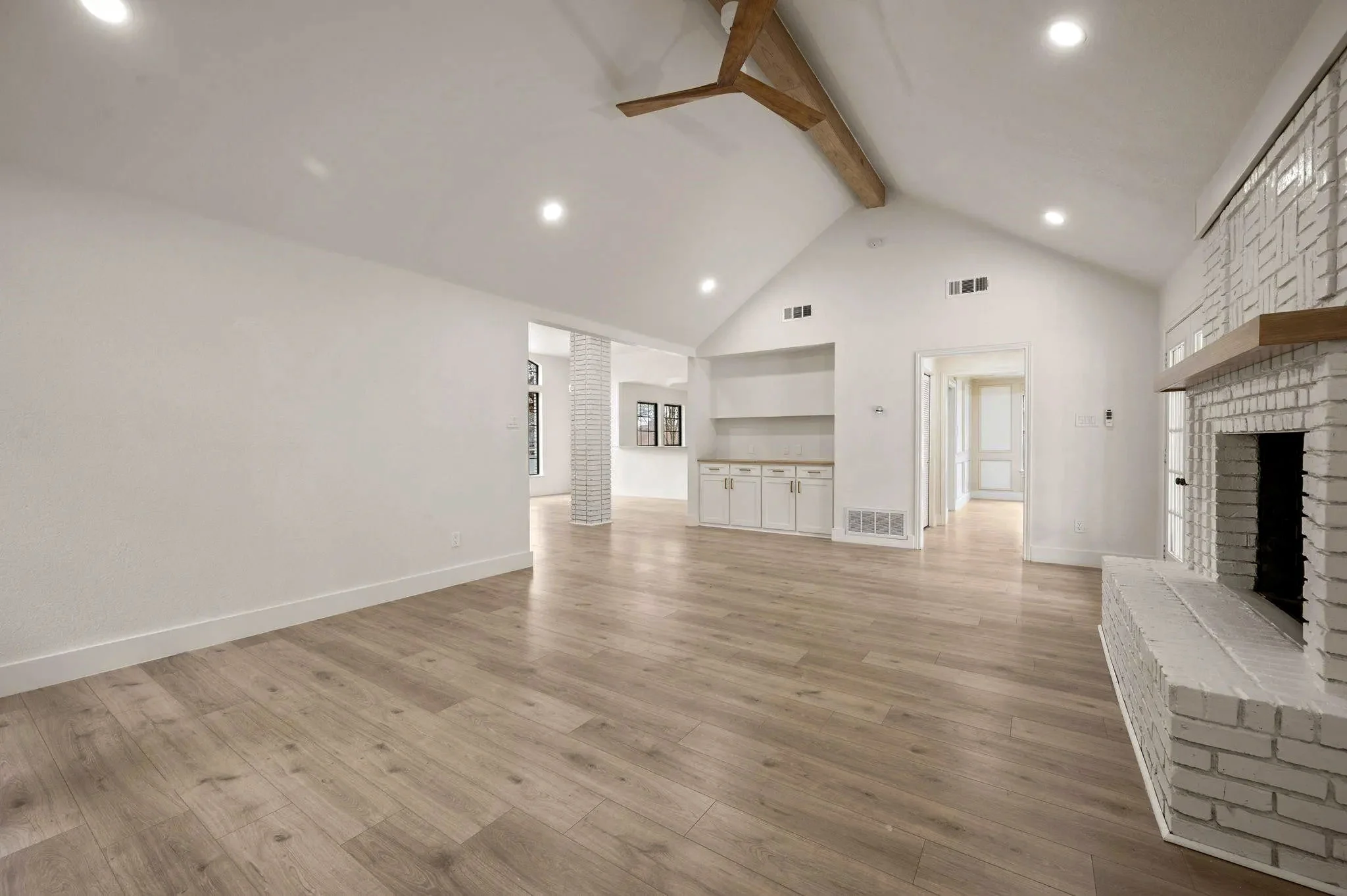 Vaulted living area with exposed wood beams, white brick fireplace, built-in cabinetry, and wide-plank flooring in Grapevine, Texas.