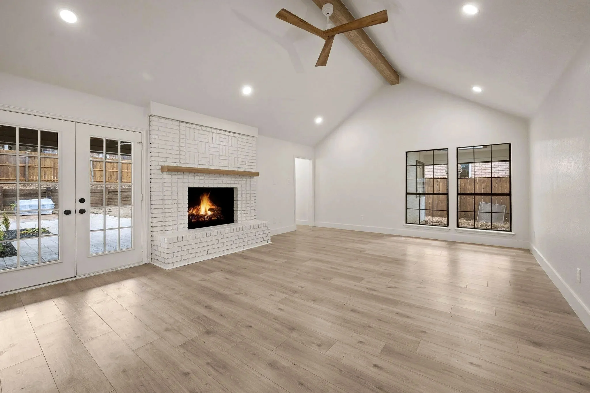 Vaulted living room with wood beams, a white brick fireplace, black-framed windows, and wide-plank flooring in Grapevine, Texas.