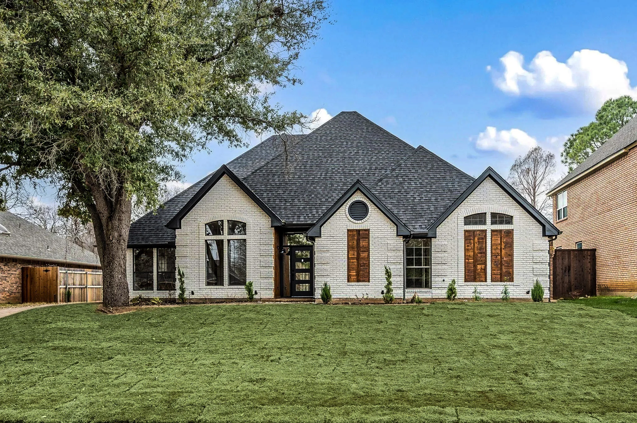 White brick home exterior with black-framed arched windows, dark roofing, a wood front door, and fresh landscaping in Grapevine, Texas.