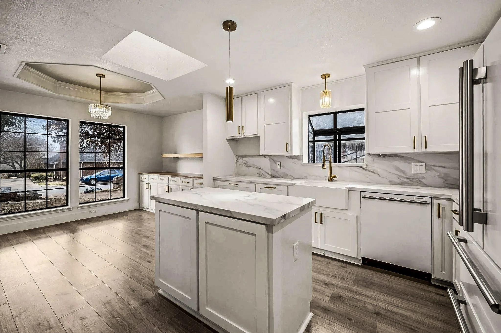 White kitchen with a center island, skylights, pendant lighting, and an adjoining breakfast room with black-framed windows in Grapevine, Texas.
