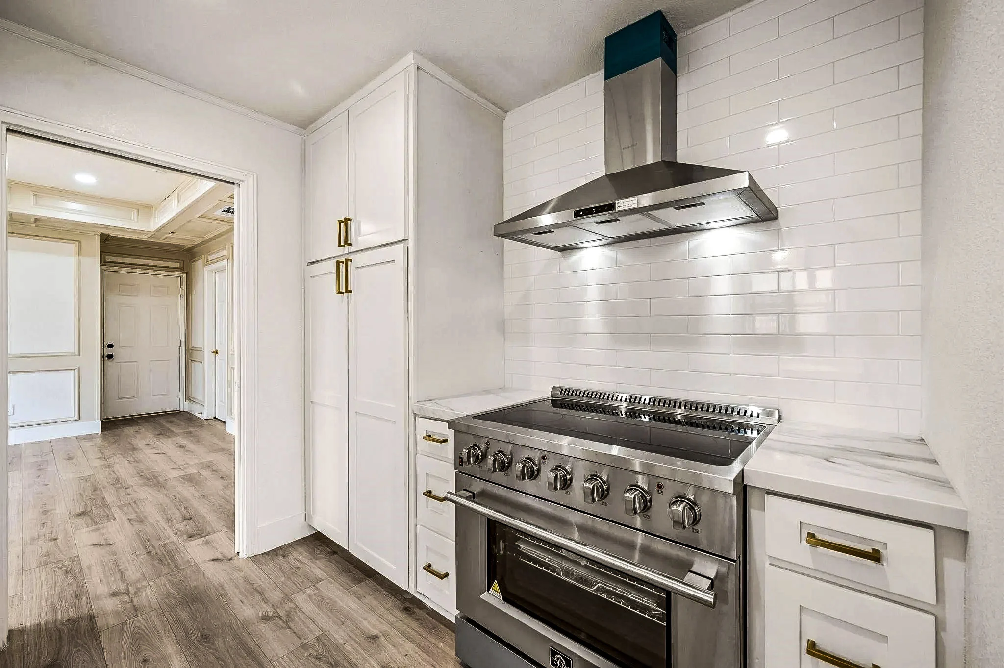 White shaker kitchen with a professional-style range, brass pot filler, marble-look backsplash, and brass hardware in Grapevine, Texas.