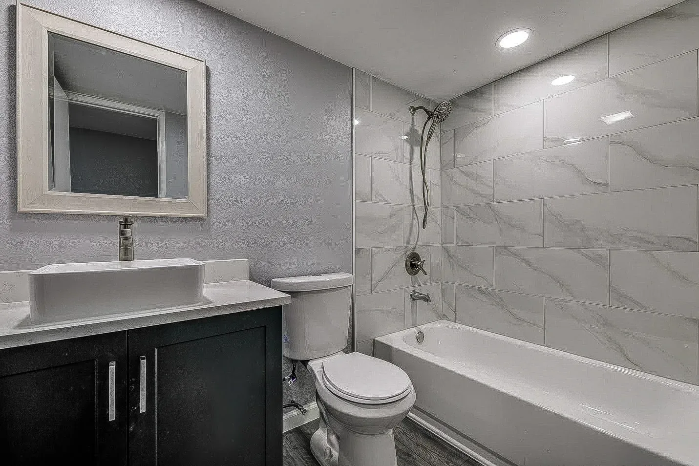 Dallas guest bathroom with dark vanity, marble-look tub surround, black fixtures, and framed mirror.