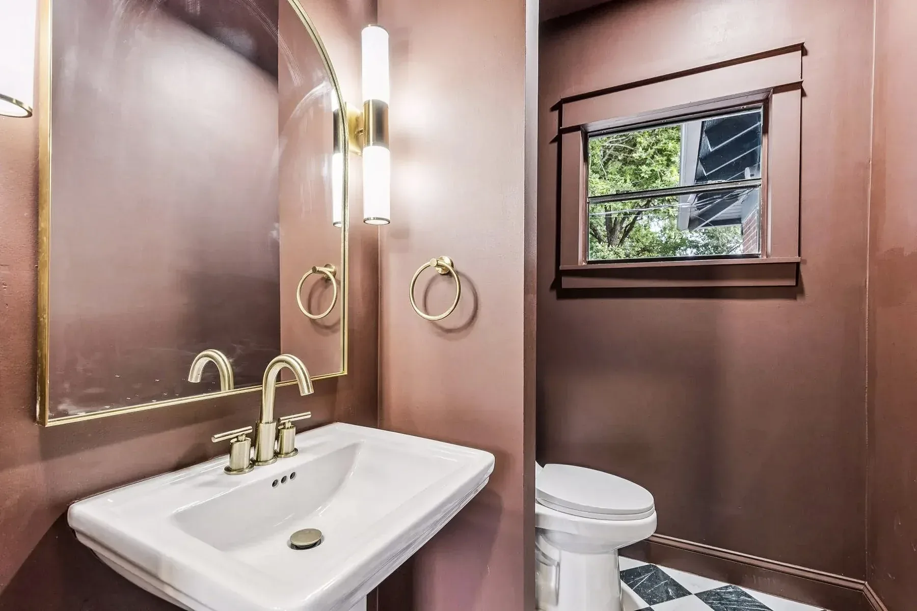 Dallas powder room with deep red walls, white pedestal sink, brass fixtures, sconces, and black window.