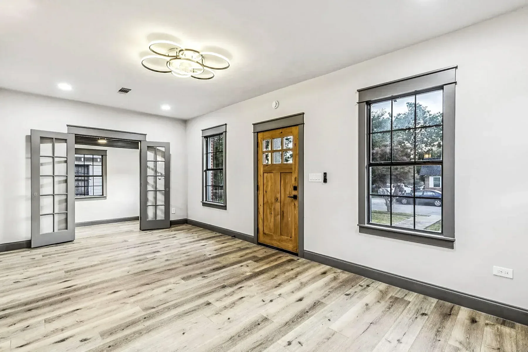 Freshly painted Dallas living room with white walls, black-framed windows, wood-look flooring, and wood front door.