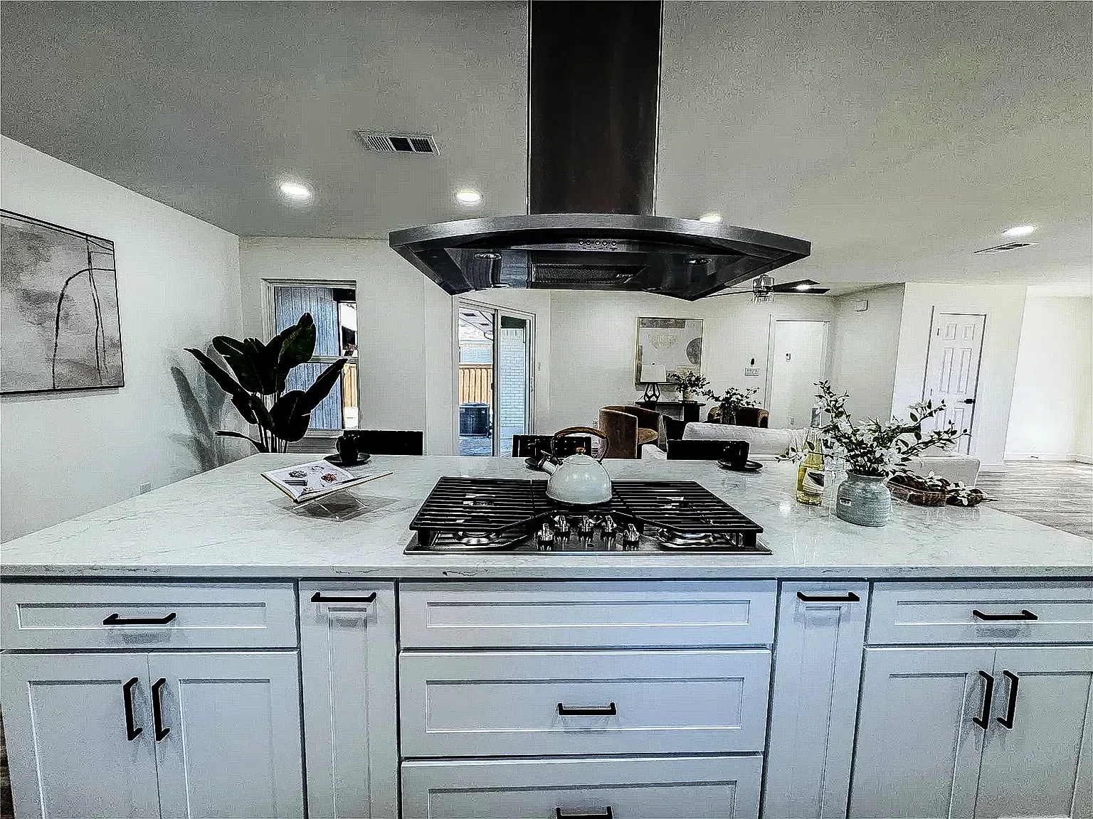 Lower Greenville kitchen island with white cabinetry, dark range hood, quartz surface, and open living space.