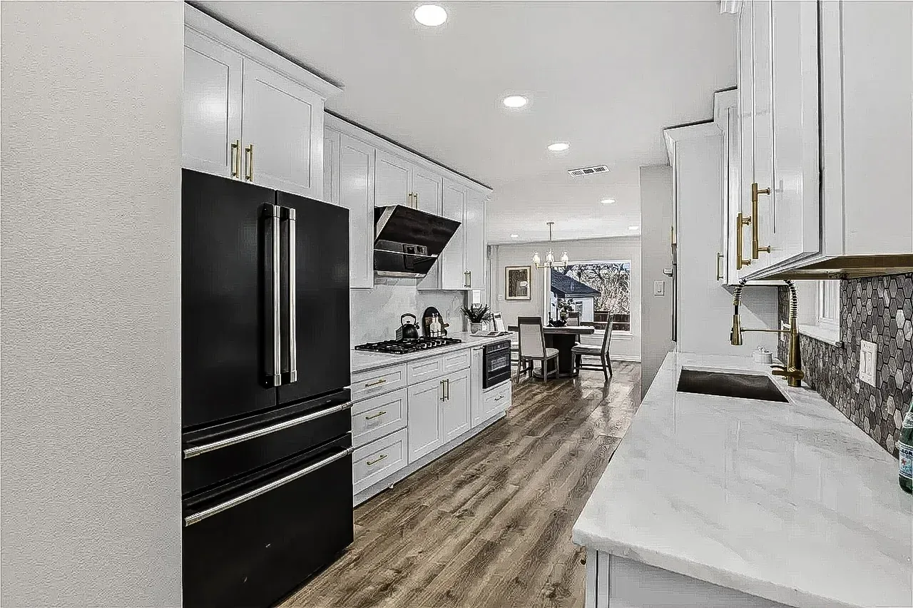 Lakewood galley kitchen with white shaker cabinets, black refrigerator, brass hardware, and dark mosaic backsplash.