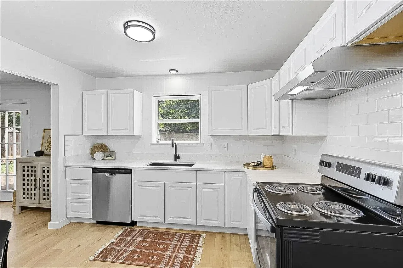 Lewisville kitchen with white cabinetry, subway tile backsplash, black sink, and stainless steel appliances.