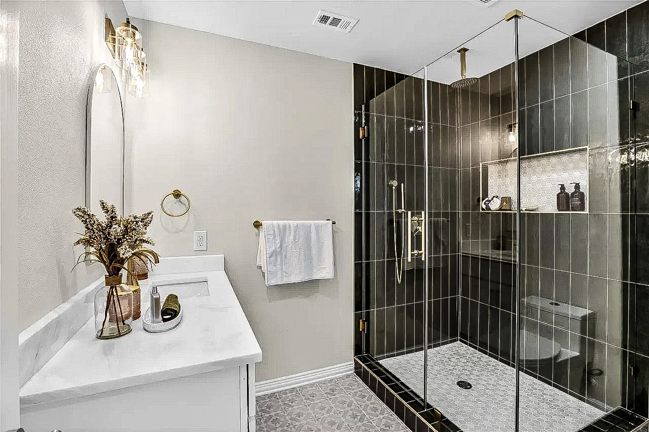 Tub and shower remodel with dark vertical tile, glass panel, brass fixtures, and white vanity in Lakewood, Dallas.
