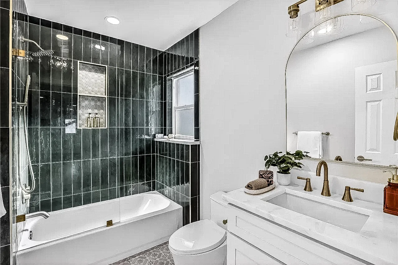 Bathroom with dark vertical shower tile, white tub, glass enclosure, brass fixtures, and white vanity in Lakewood, Dallas.