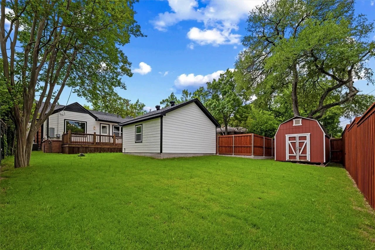 Fresh green sod across the backyard with a detached garage, accessory structure, mature shade trees, and red privacy fence in Lakewood, Dallas, Texas.