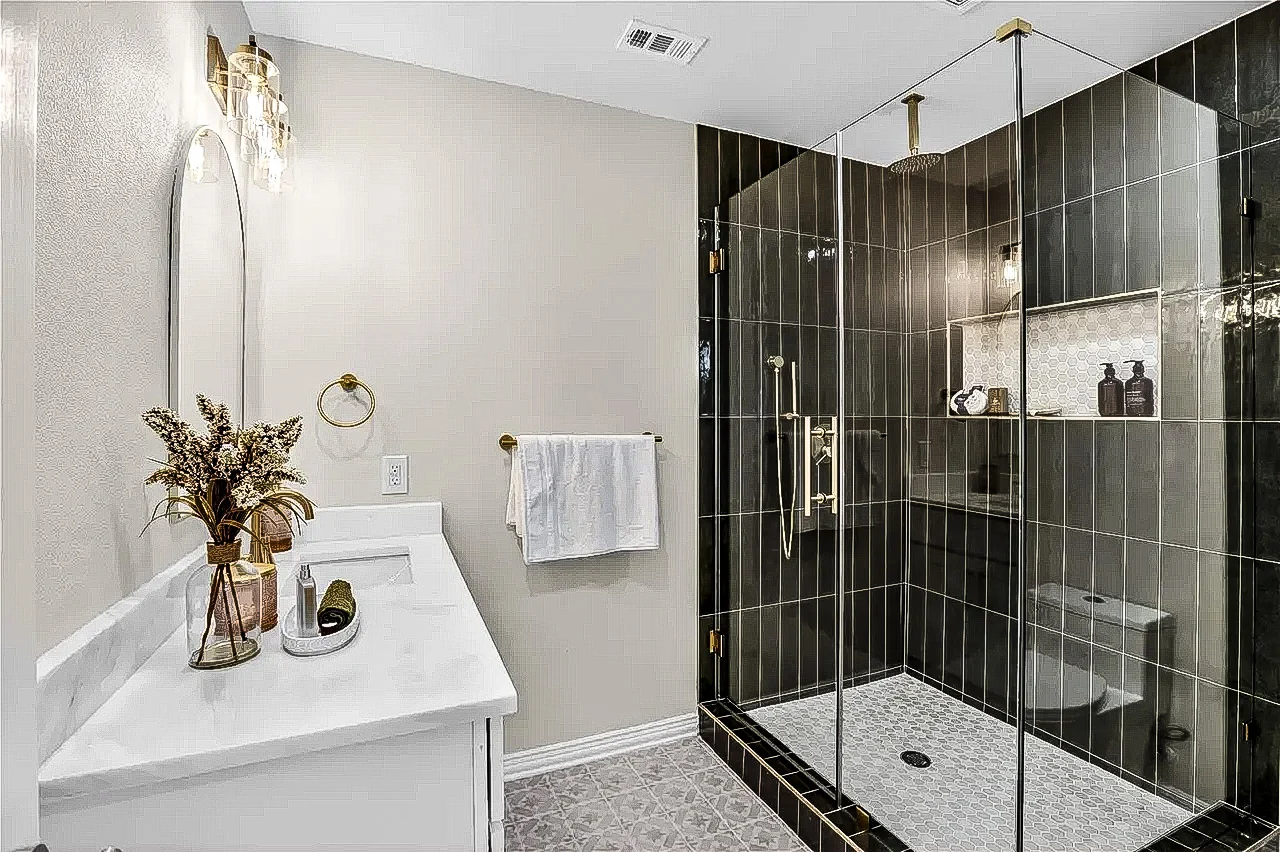 Frameless glass shower with glossy black tile, black fixtures, built-in niche, white walls, and a white vanity in Lakewood, Dallas, Texas.