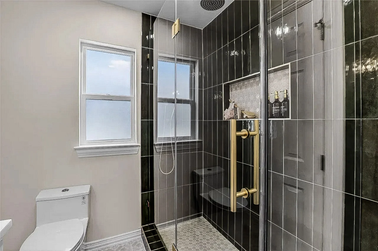Bathroom with glossy black tile, frameless glass shower, black fixtures, white vanity, and bright natural light in Lakewood, Dallas, Texas.