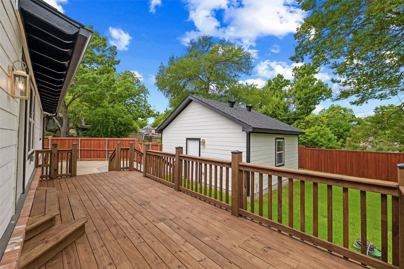 Backyard view across the new wood deck toward the detached garage and accessory structure with coordinated siding and trim in Lakewood, Dallas, Texas.