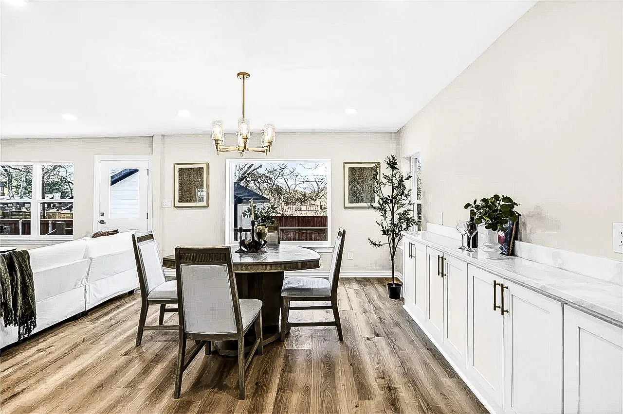Dining room with a long white built-in buffet, brass chandelier, light wood-look flooring, and large windows in Lakewood, Dallas, Texas.