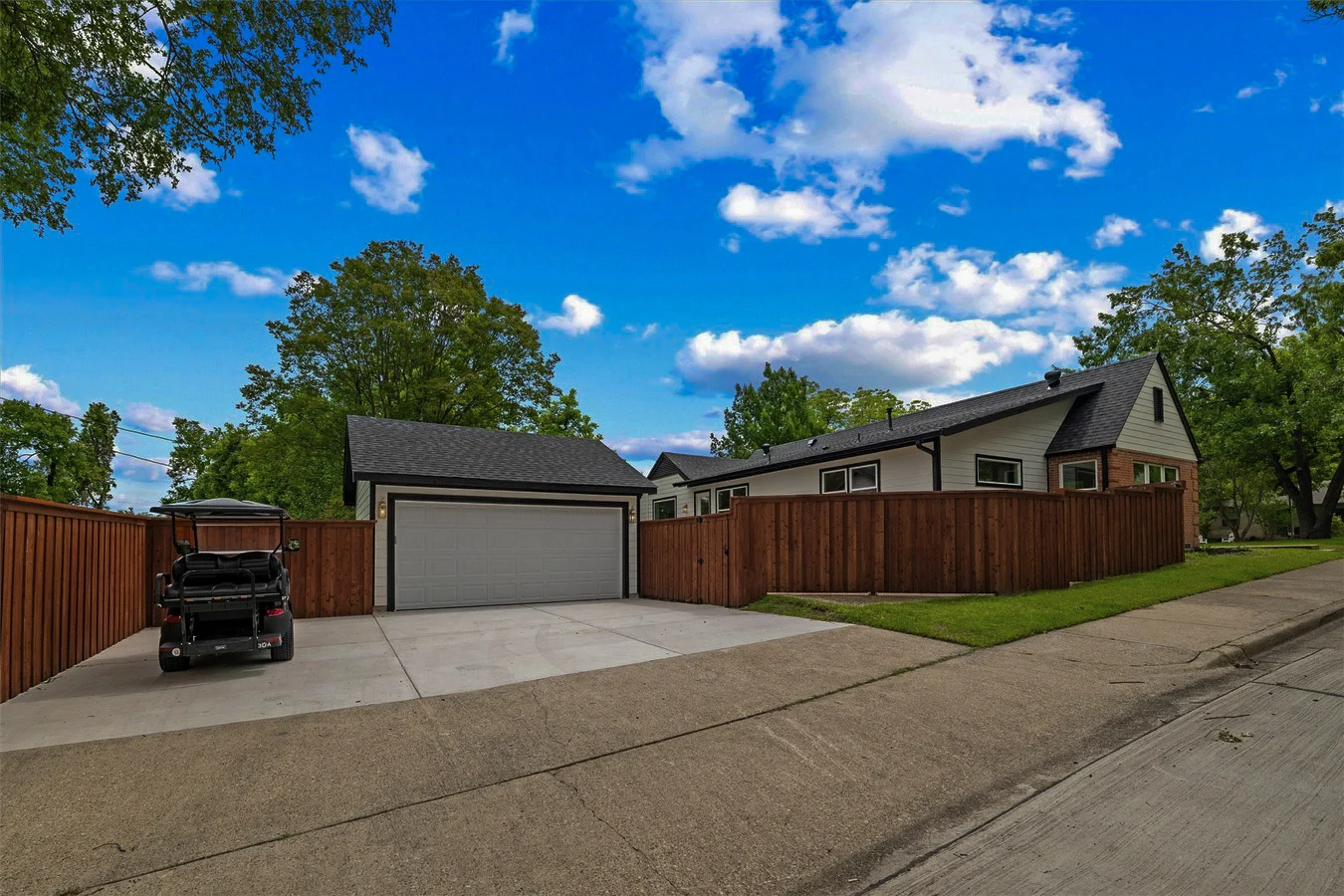 Wide driveway with a new wood privacy fence, detached garage, coordinated exterior finishes, and mature trees in Lakewood, Dallas, Texas.
