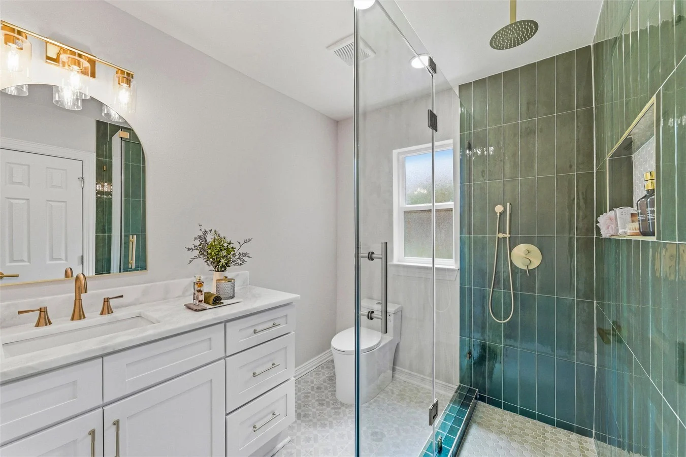 Primary bathroom with glossy green shower tile, white double vanity, brass fixtures, glass shower, and bright natural light in Lakewood, Dallas, Texas.