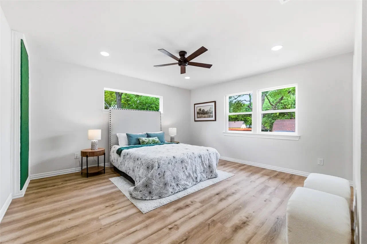Primary bedroom with a deep green accent wall, white ceiling, pale flooring, black ceiling fan, and multiple windows in Lakewood, Dallas, Texas.