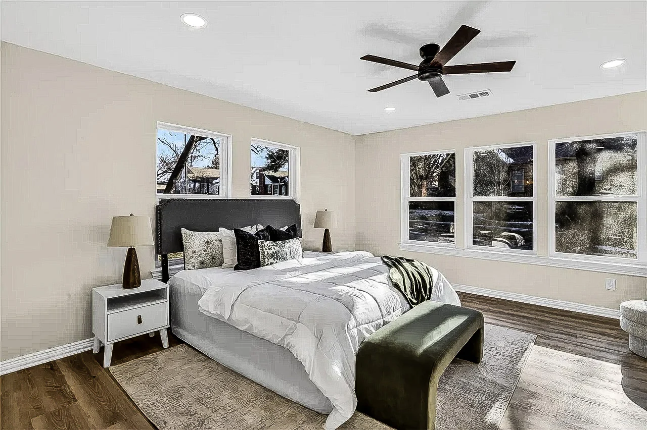 Primary bedroom with pale flooring, white walls, black ceiling fan, multiple windows, and staged furnishings in Lakewood, Dallas, Texas.