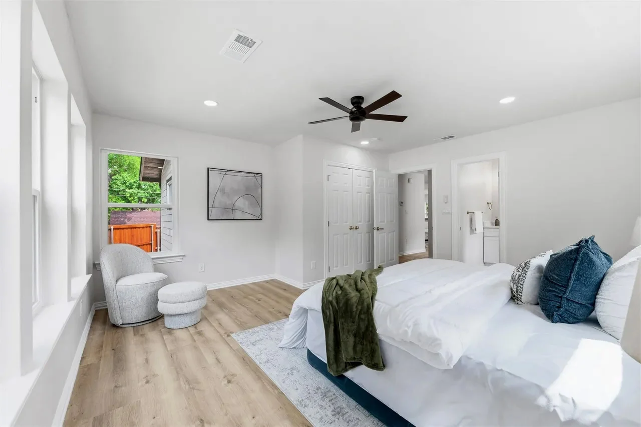 Secondary bedroom with pale flooring, white walls, black ceiling fan, large windows, and staged furnishings in Lakewood, Dallas, Texas.