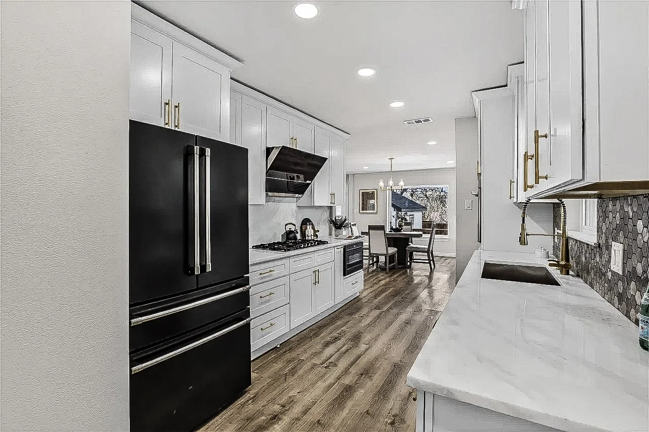 White kitchen with a broad island, black appliances, brass hardware, patterned backsplash, and open sightlines to the living area in Lakewood, Dallas, Texas.