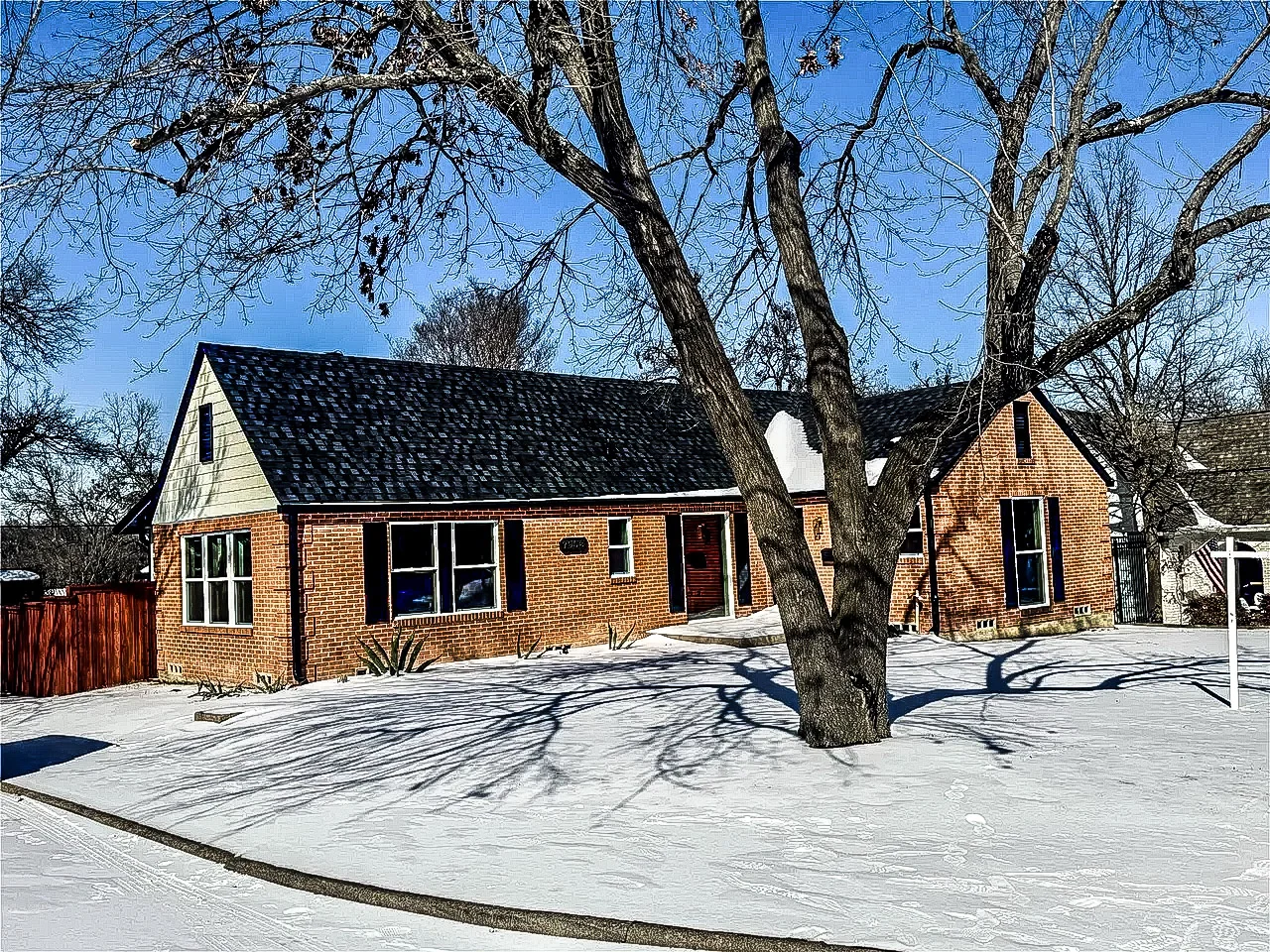 Red brick Lakewood home with black replacement windows, dark roofing, mature trees, and a snow-covered front yard in Lakewood, Dallas, Texas.