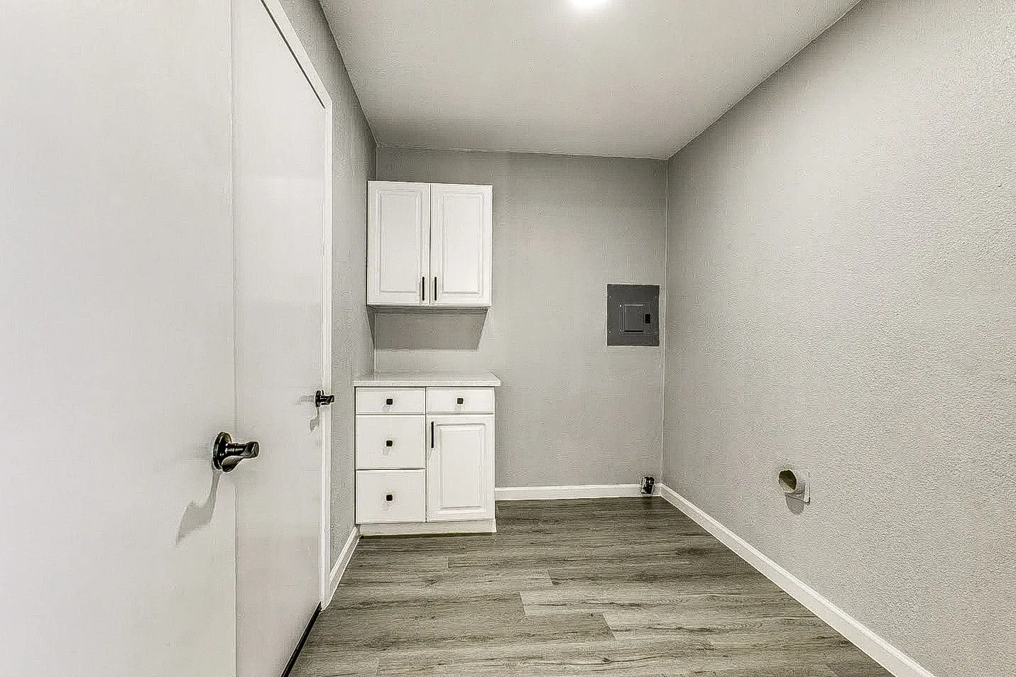 Dallas laundry room with white upper and lower cabinets, utility counter, and wood-look flooring.