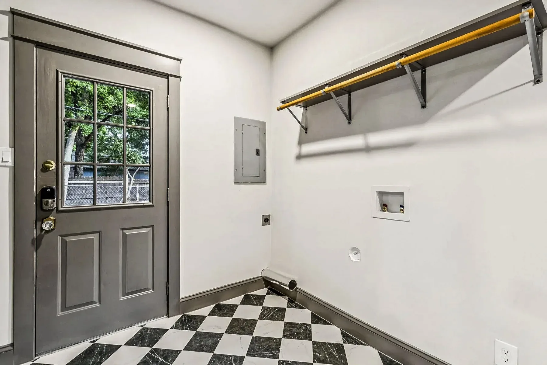 Dallas custom laundry room with black-and-white checkerboard floor, dark door trim, shelf, and brass hanging rod.
